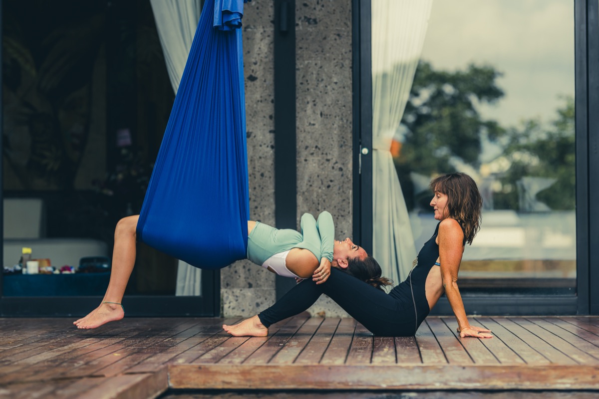 A client cocooned in the blue Somatic Swing, arching in a supported backbend on the deck of the Aum Dome