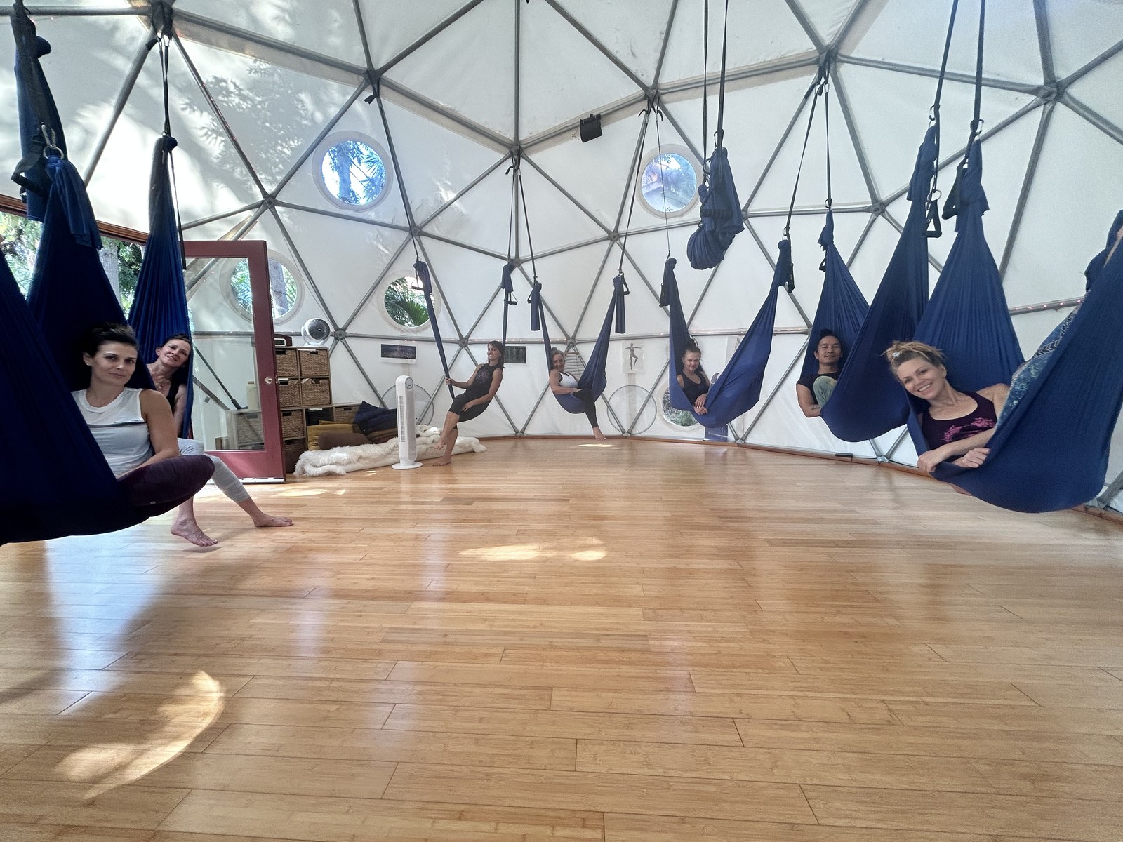 Eight or nine practitioners each seated in their own swing around the edge of the Aum Dome, all turned toward the camera